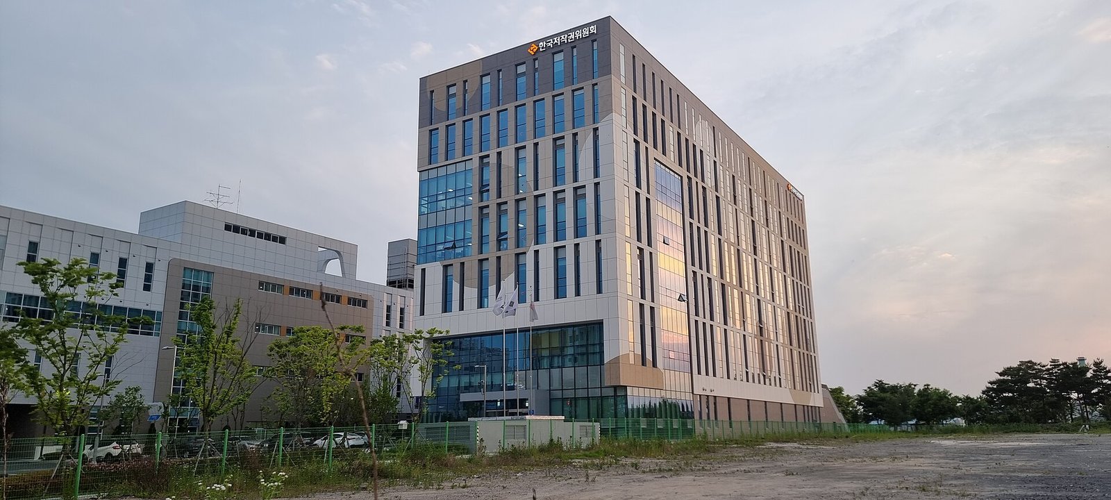 해 질 무렵 경남 진주의 한국저작권위원회 본사 건물. 회색과 베이지색 외벽의 10층 안팎 건물 꼭대기에 기관 이름이 보인다