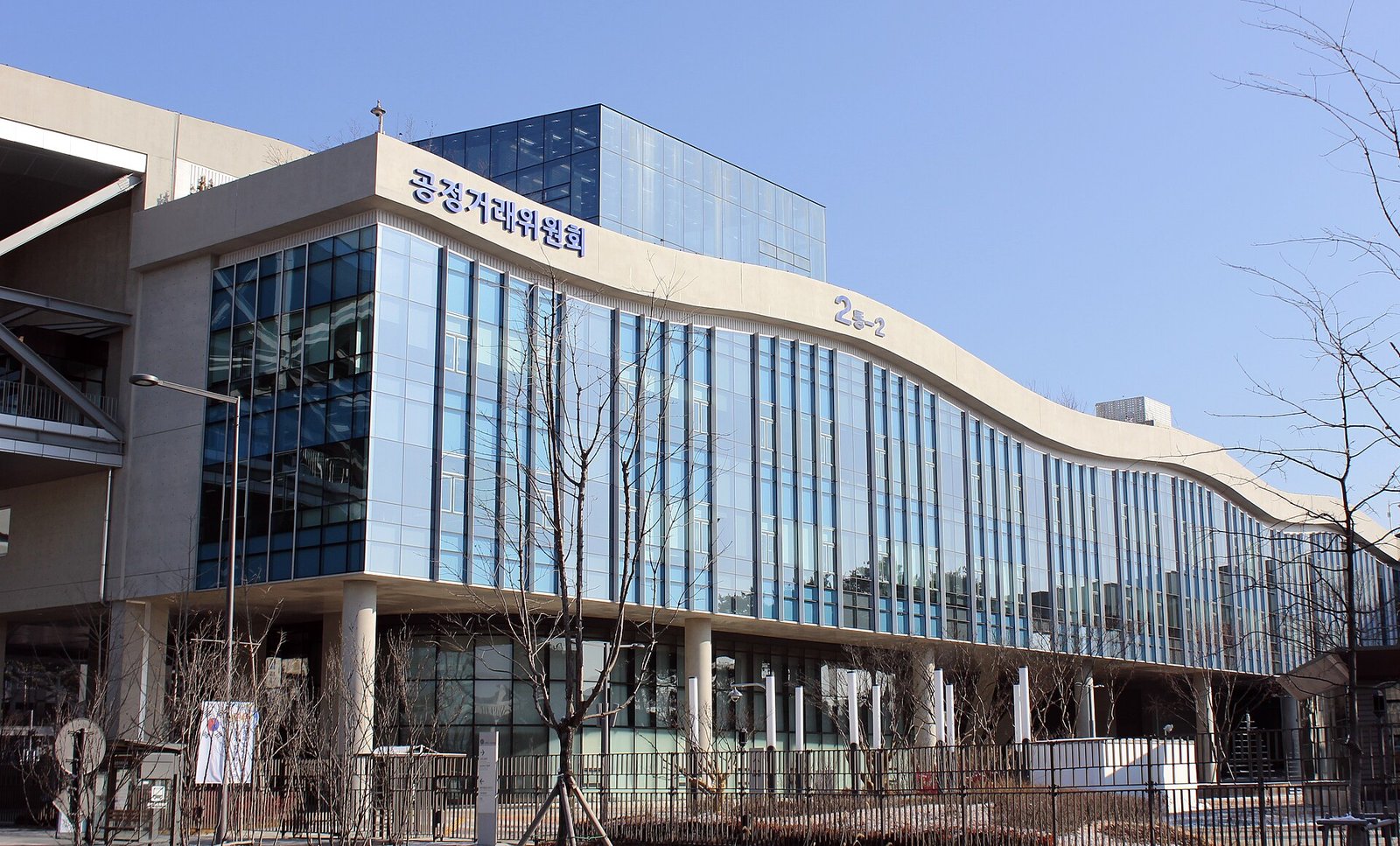 맑은 하늘 아래 정부세종청사의 공정거래위원회 건물. 유리창이 길게 이어진 물결 모양 외벽에 '공정거래위원회' 글자가 보인다