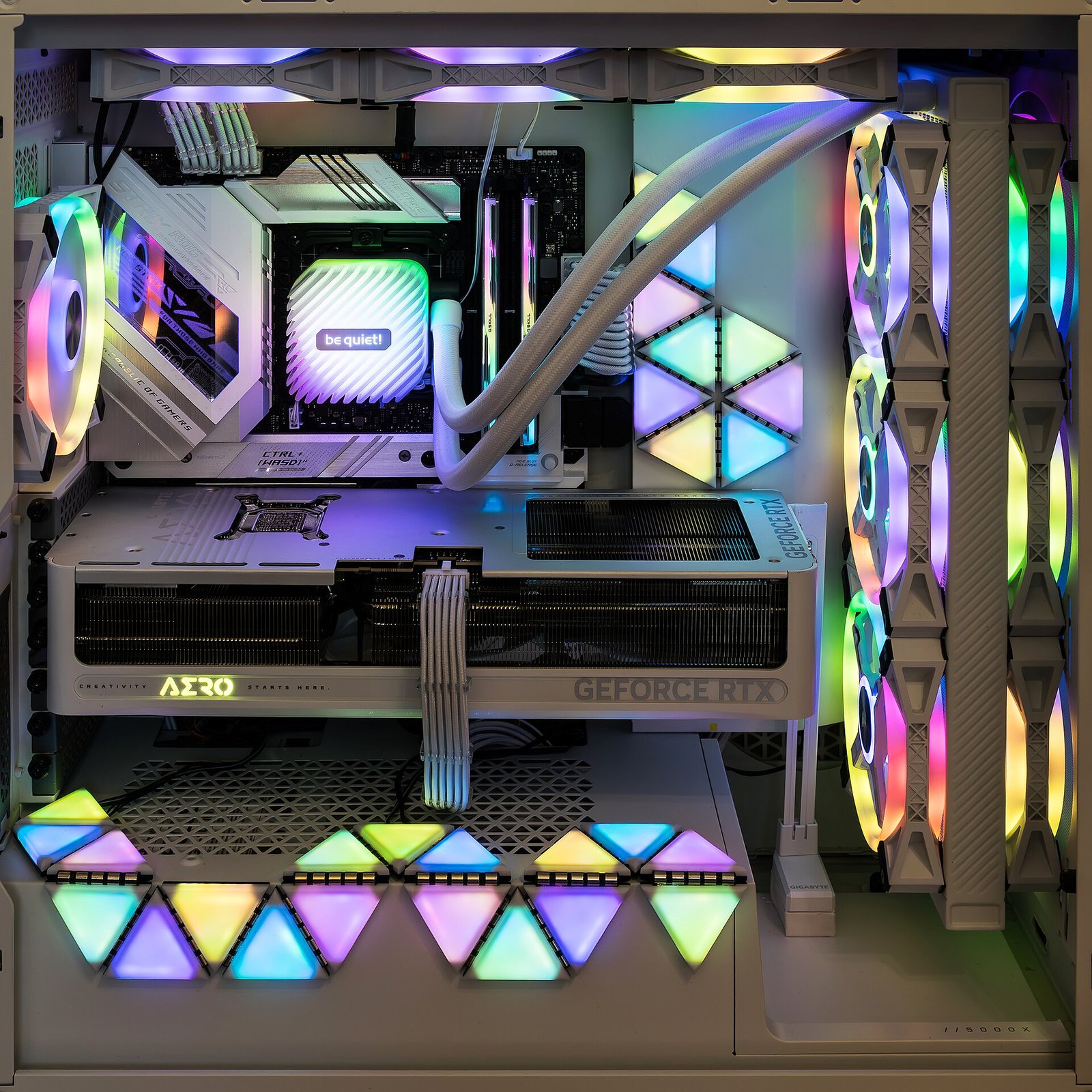 흰색 PC 케이스 내부. 메인보드에 램 두 개가 꽂혀 있고, 수랭 쿨러와 그래픽카드, 무지갯빛 조명 팬이 둘러싸고 있다