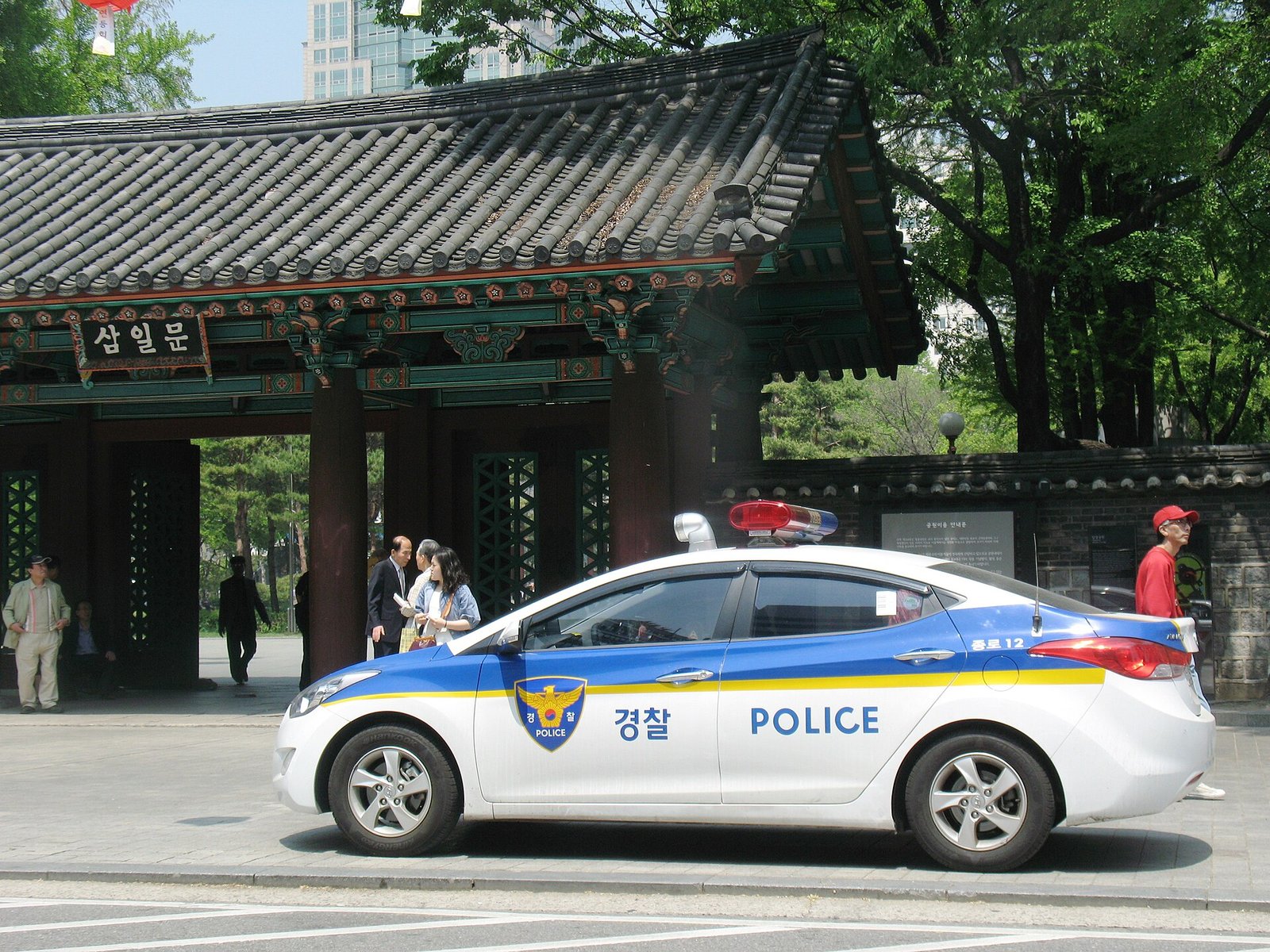 서울 탑골공원 삼일문 앞에 흰색과 파란색의 경찰 순찰차가 서 있고 주변을 사람들이 지나간다
