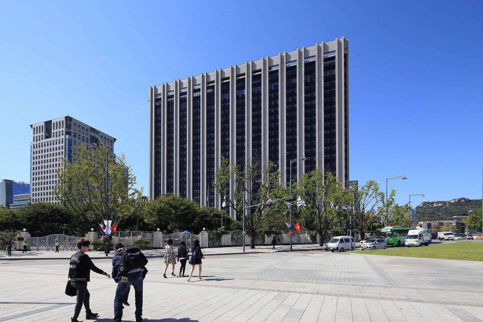 맑은 가을날 정부서울청사 본관 앞 광장을 젊은 사람들이 걸어가고 있다. 뒤로 세로줄 무늬의 높은 청사 건물과 은행나무가 보인다
